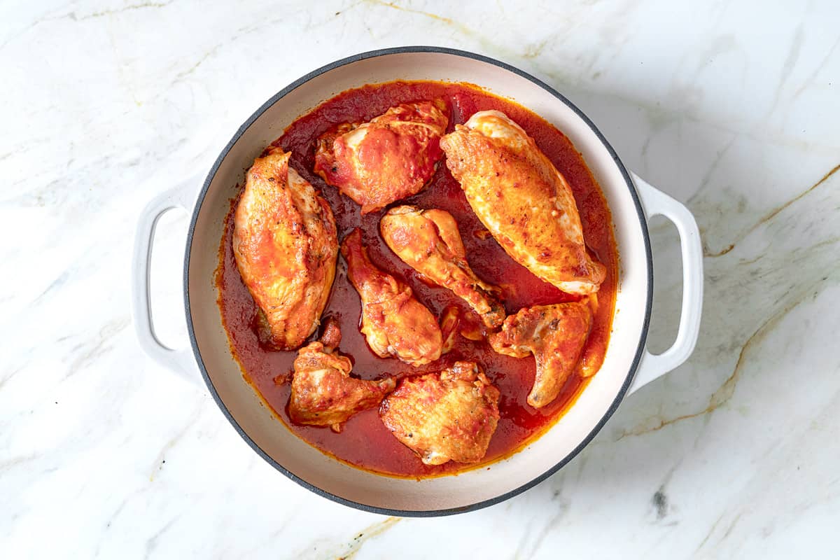 browned pieces of chicken in s skillet braising in a tomato sauce.