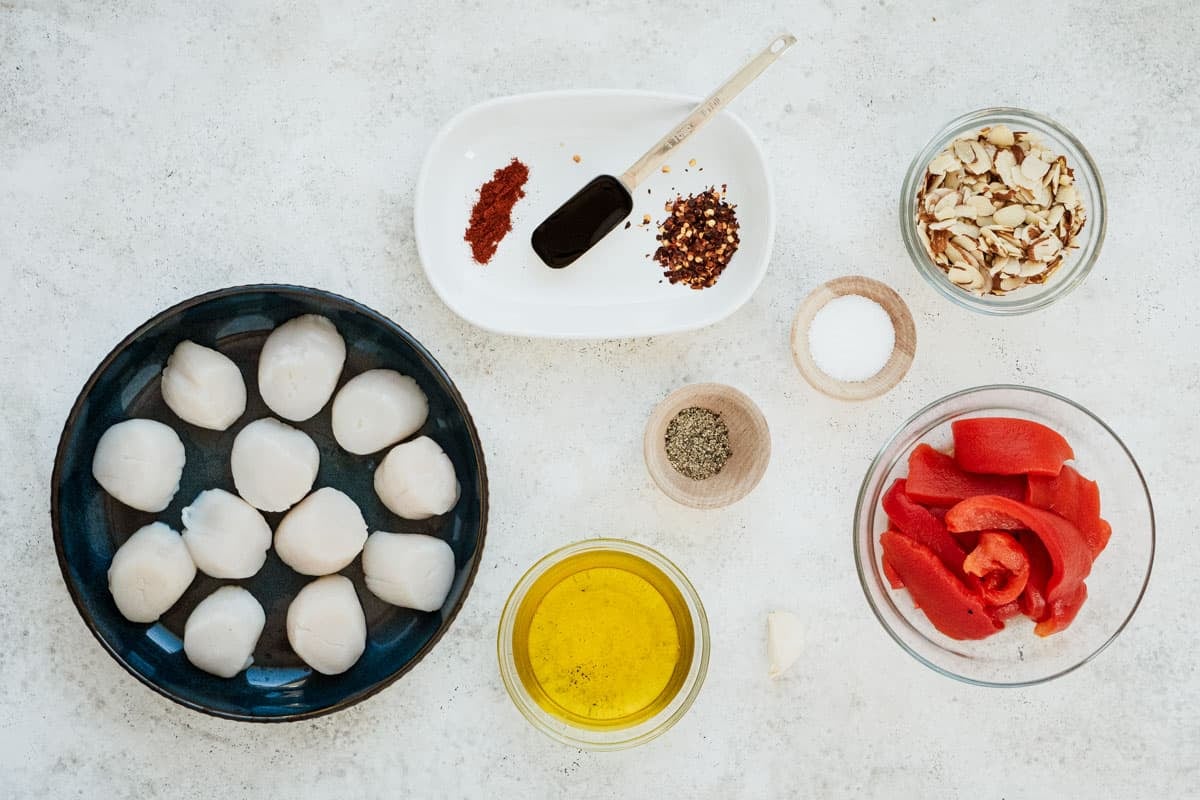 ingredients for seared scallops including large scallops, almonds, roasted red bell peppers, olive oil, garlic, red chili flakes, sweet paprika, salt and black pepper.