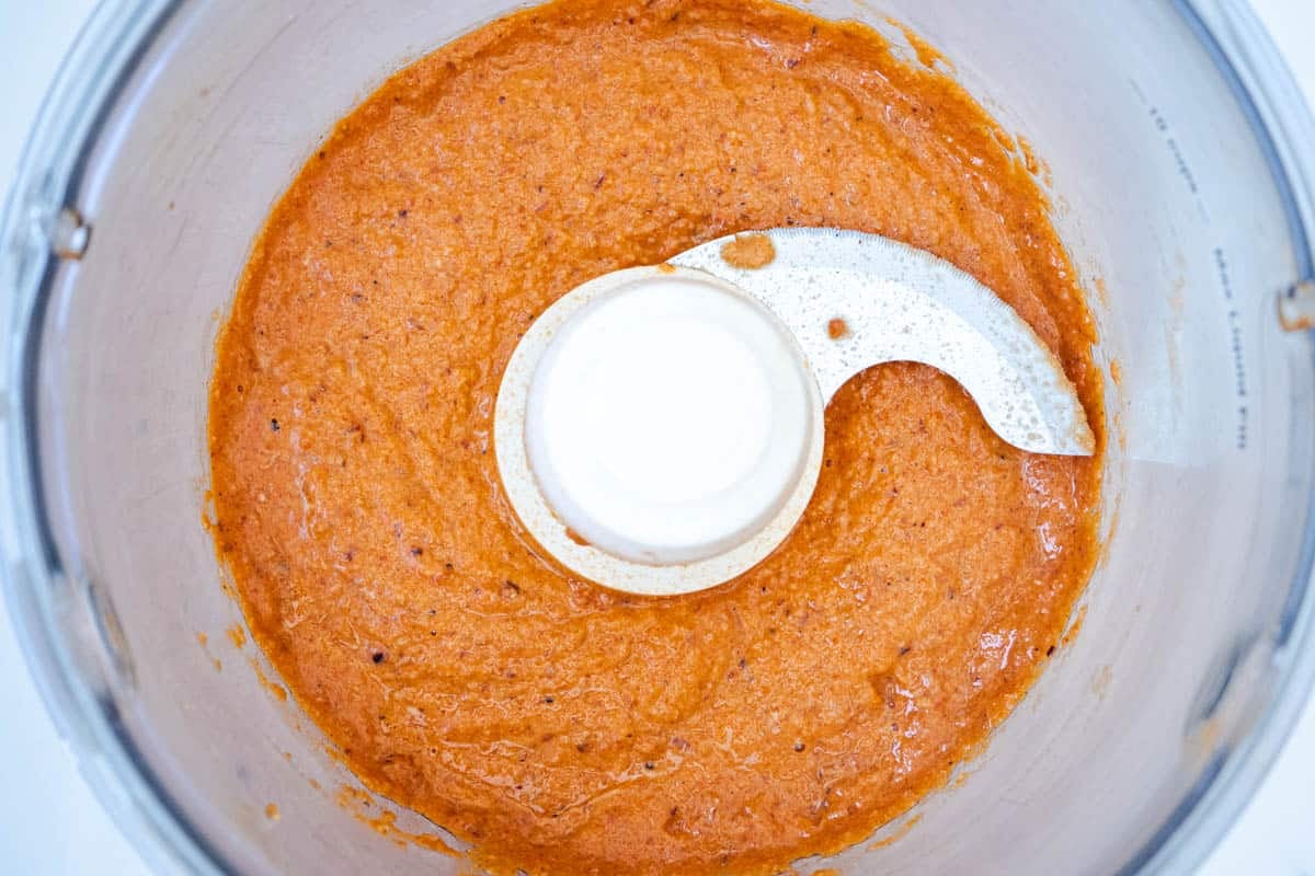 red pepper sauce in the bowl of a food processor with a blade.