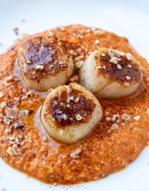 a plate of seared scallops served on a spicy red pepper sauced and garnished with crushed almonds.