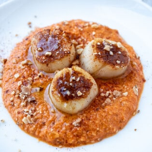 a plate of seared scallops served on a spicy red pepper sauced and garnished with crushed almonds.