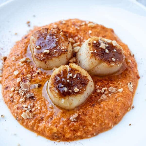 a plate of seared scallops served on a spicy red pepper sauced and garnished with crushed almonds.