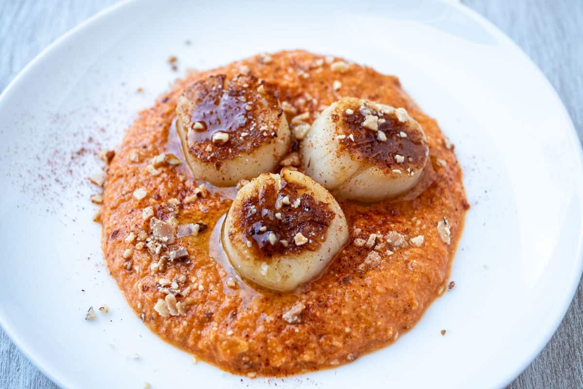 a plate of seared scallops served on a spicy red pepper sauced and garnished with crushed almonds.