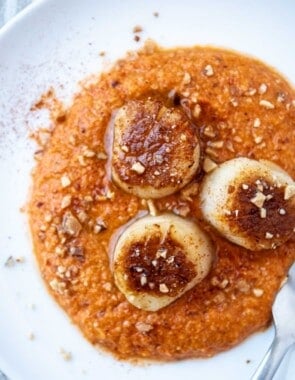 An overhead photo of a plate of seared scallops served on a spicy red pepper sauced and garnished with crushed almonds.