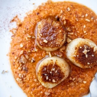 An overhead photo of a plate of seared scallops served on a spicy red pepper sauced and garnished with crushed almonds.