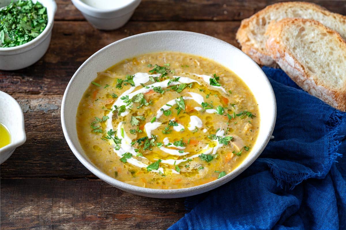 soupe jo in a bowl garnished with half and half and chopped parsley, surrounded by small bowls of olive oil, chopped parsley and half and half, and slices of crusty bread.