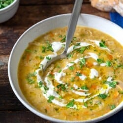 soupe jo in a bowl with a spoon garnished with half and half and chopped parsley, surrounded by small bowls of chopped parsley and half and half, and slices of crusty bread.