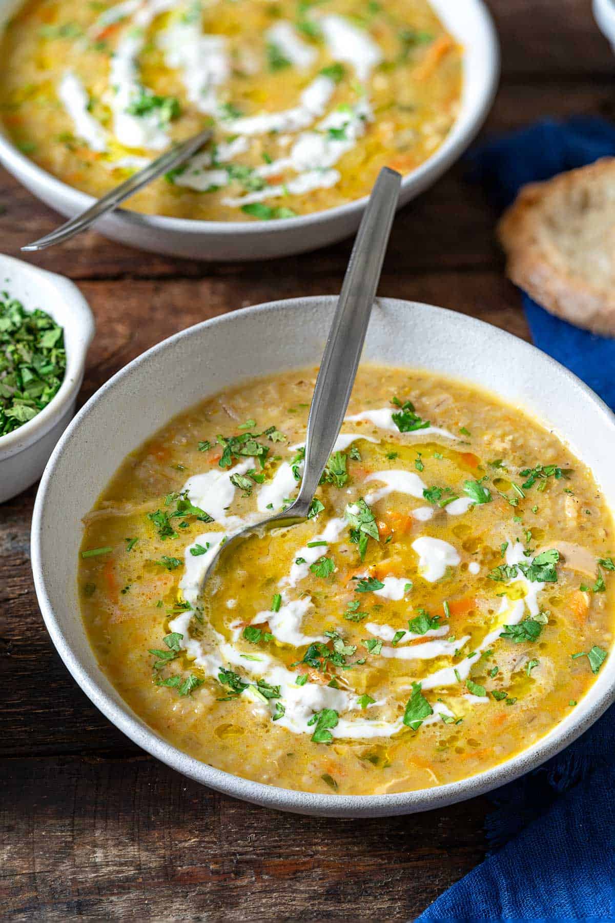 two bowls of soupe jo with spoons garnished with half and half and chopped parsley, surrounded by a small bowl of chopped parsley, and a slice of crusty bread.