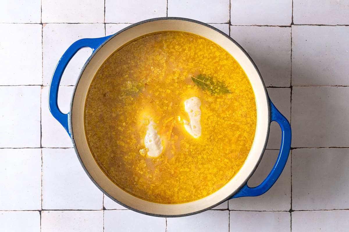 barley, vegetables, bay leaves and chicken breast simmering in a pot of chicken stock.