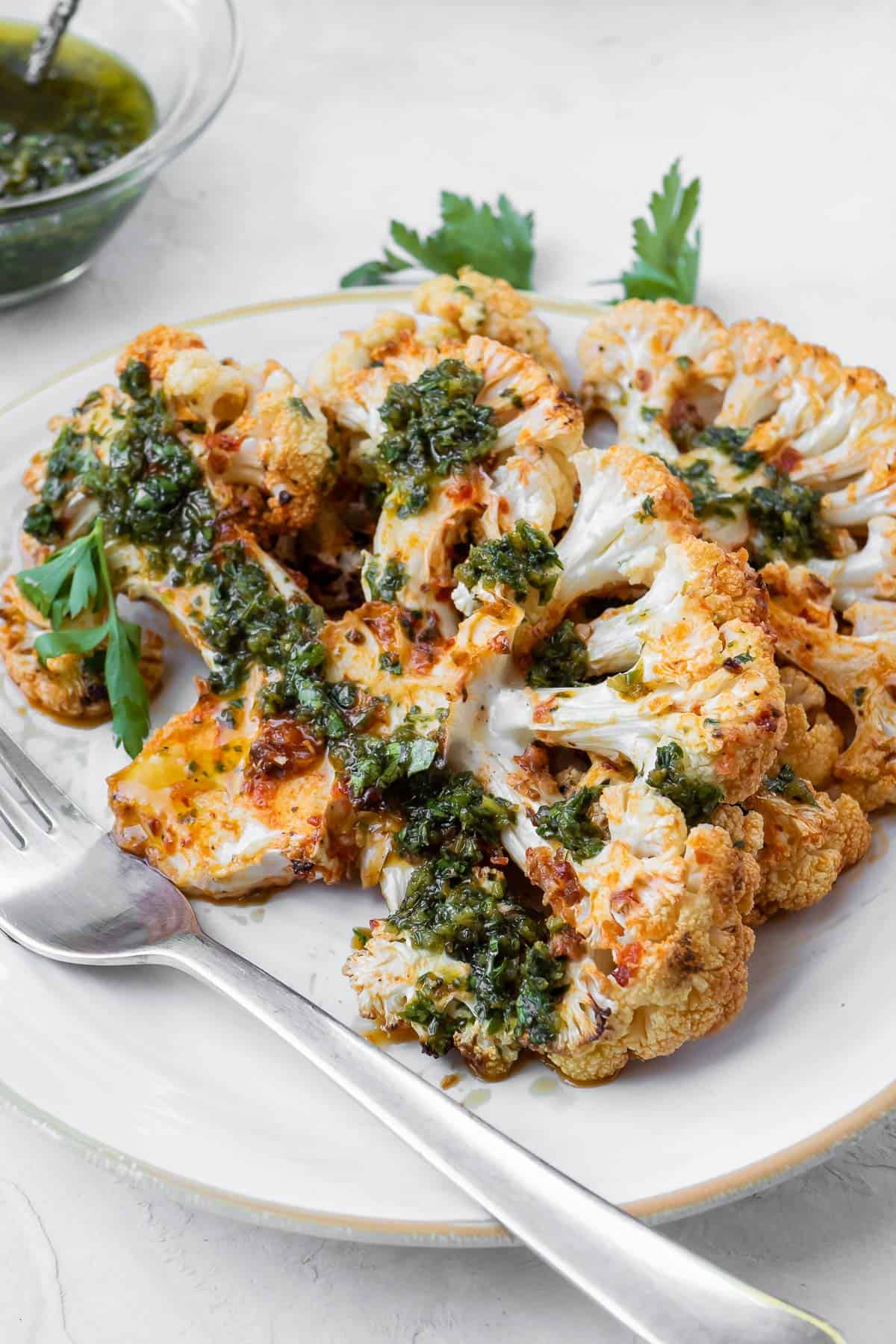 Zoomed in Side shot of a cauliflower steak on a white plate with a metal fork.