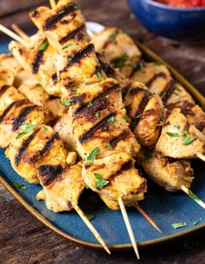 a close up of 6 joojeh kabobs on a serving platter next to a small bowl of parsley.