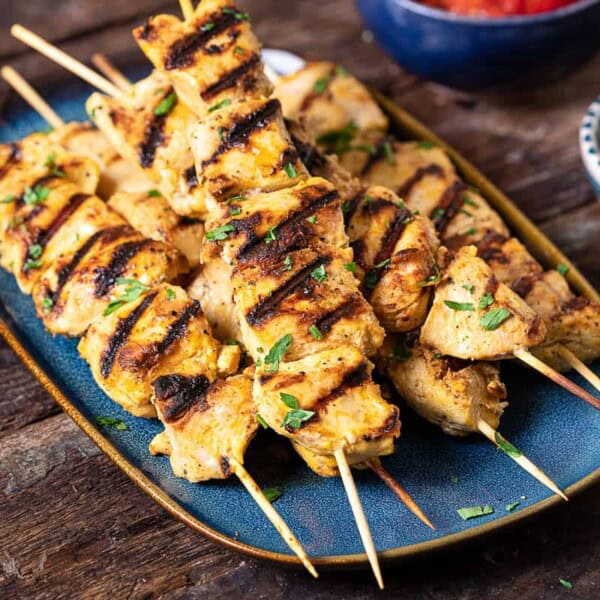 a close up of 6 joojeh kabobs on a serving platter next to a small bowl of parsley.