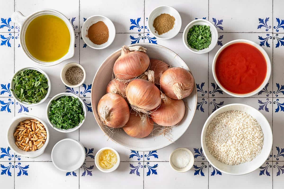 ingredients for stuffed onions including onions, rice, pine nuts, garlic, olive oil tomato puree, salt, pepper, cumin, cinnamon, pine nuts, parsley, mint, and white vinegar. 