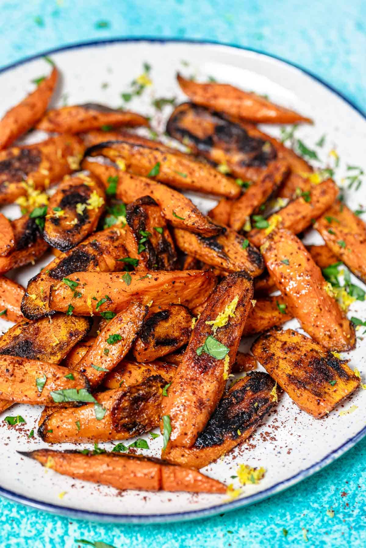 a close up of roasted carrots with sumac garnished with lemon zest and parsley on a serving plate.
