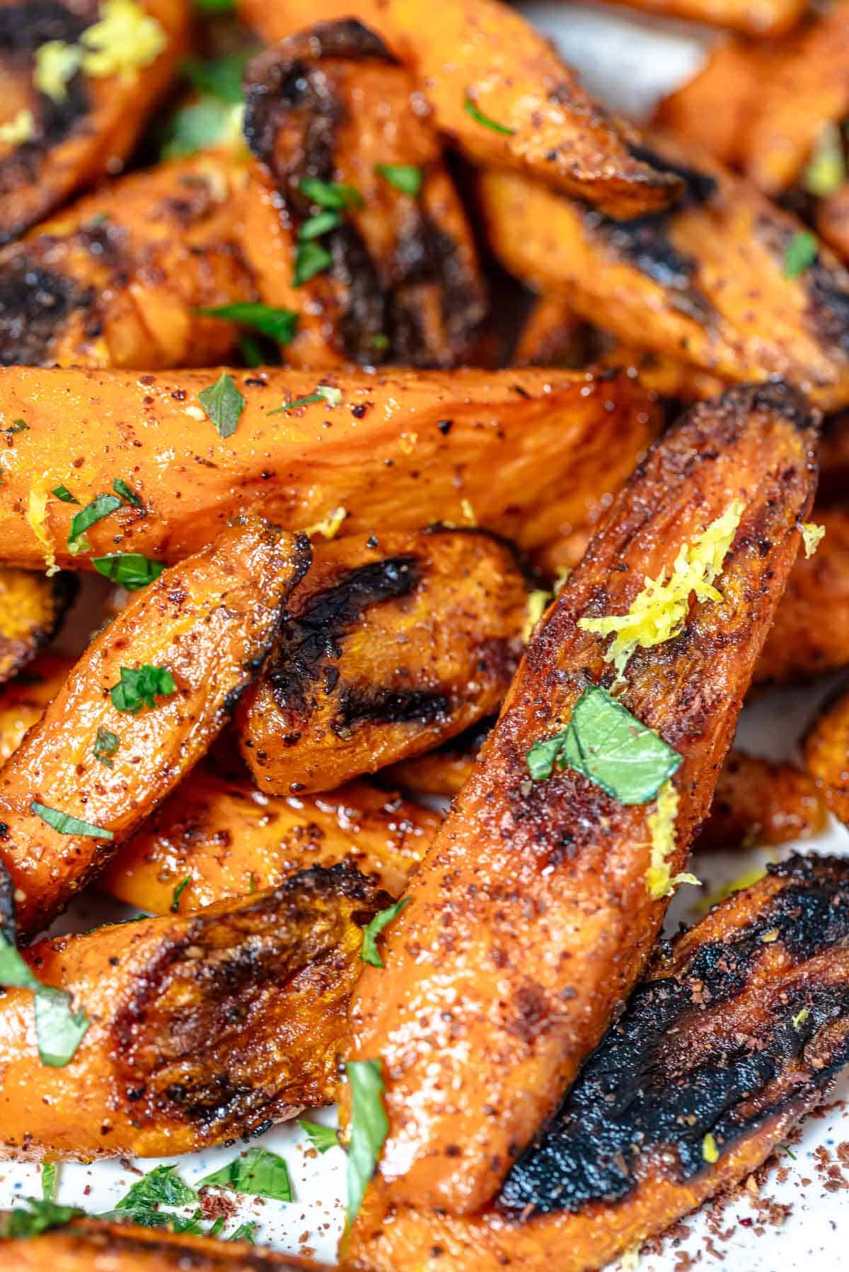 a close up of roasted carrots with sumac garnished with lemon zest and parsley.