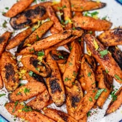 roasted carrots with sumac garnished with lemon zest and parsley on a serving plate.