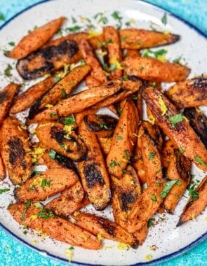 roasted carrots with sumac garnished with lemon zest and parsley on a serving plate.