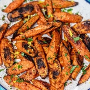 roasted carrots with sumac garnished with lemon zest and parsley on a serving plate.