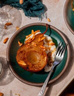 Teal plate with a large spoonful of ricotta cheese, a baked pear resting with its cut side facing up, and candied almonds sprinkled over top. It's all finished with a drizzle of honey.