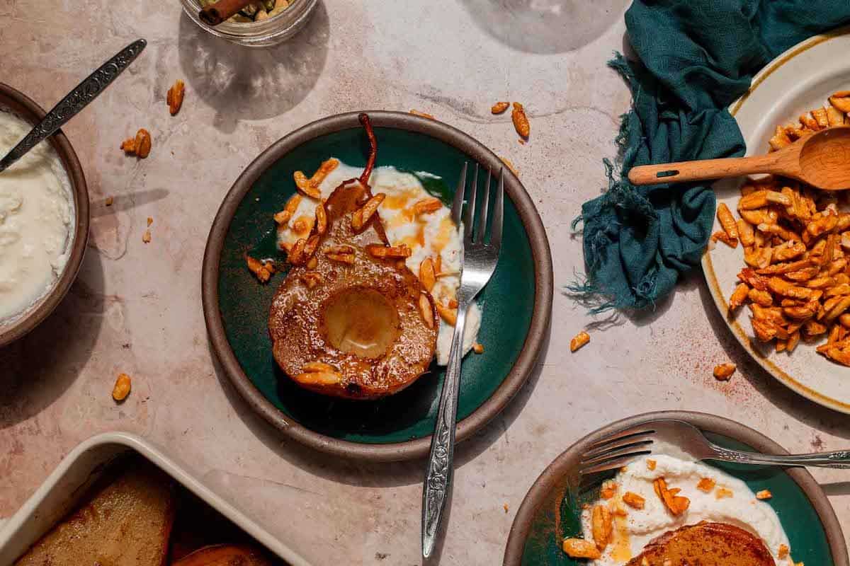 Overhead shot of a teal bowl with ricotta cheese, a baked pear, and candied almonds sprinkled over top.