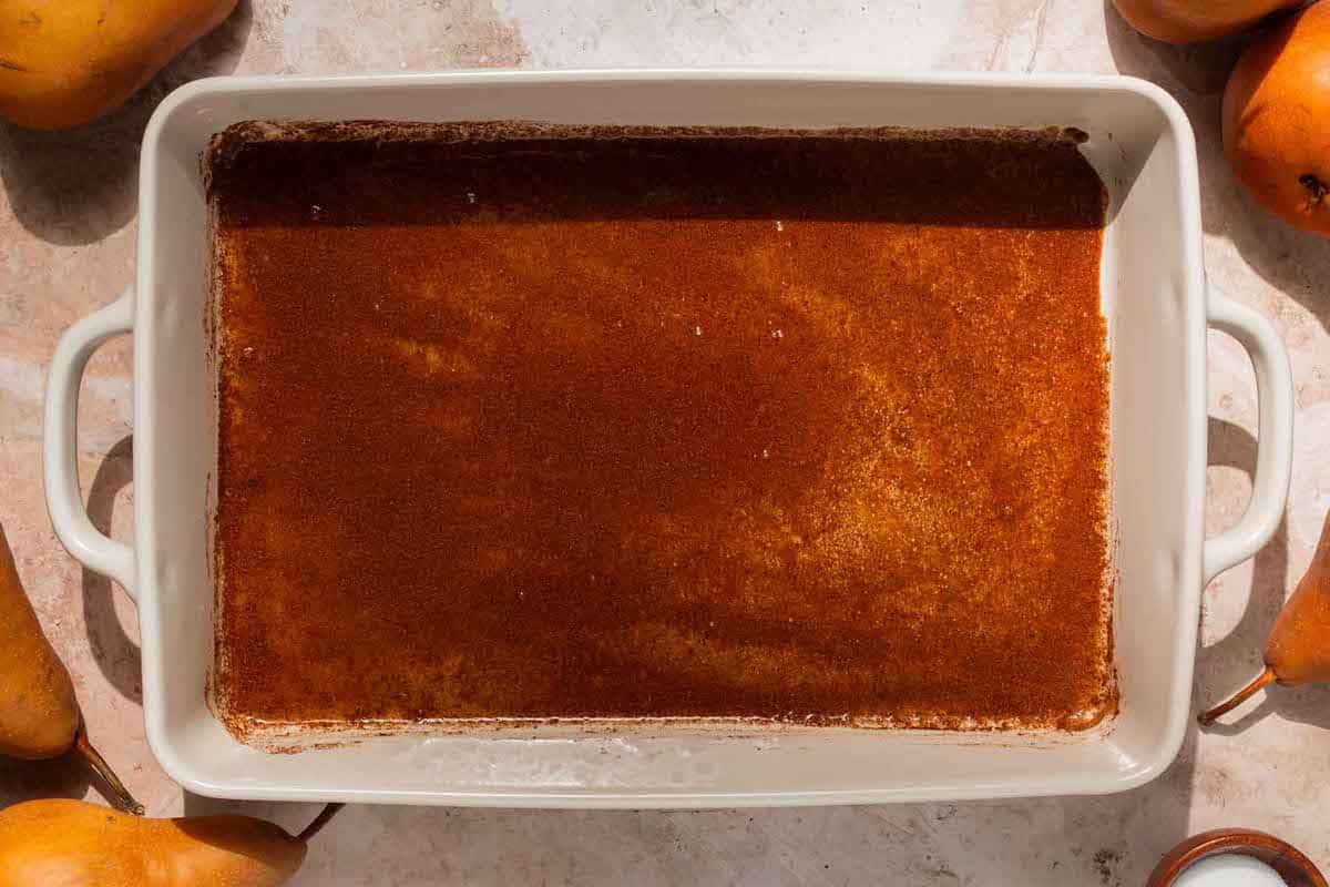 a white baking dish that's lined at the bottom with brown sugar, cinnamon, cardamom, cloves, nutmeg, juice from half a lemon, and almond extract.