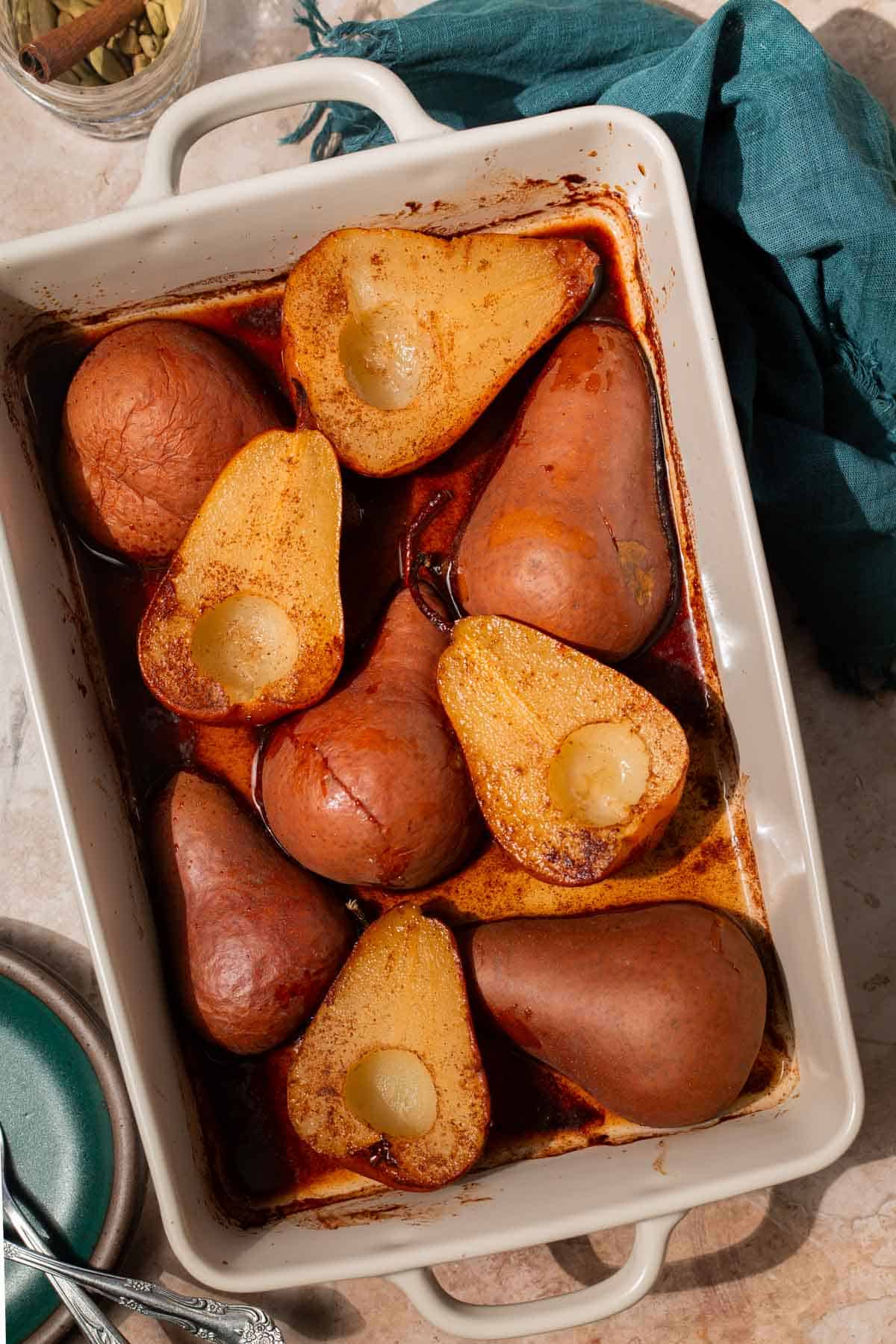 Baked pears in a white baking dish with half of the pears cut-side down. Half of the pears are flipped to show the golden edges.