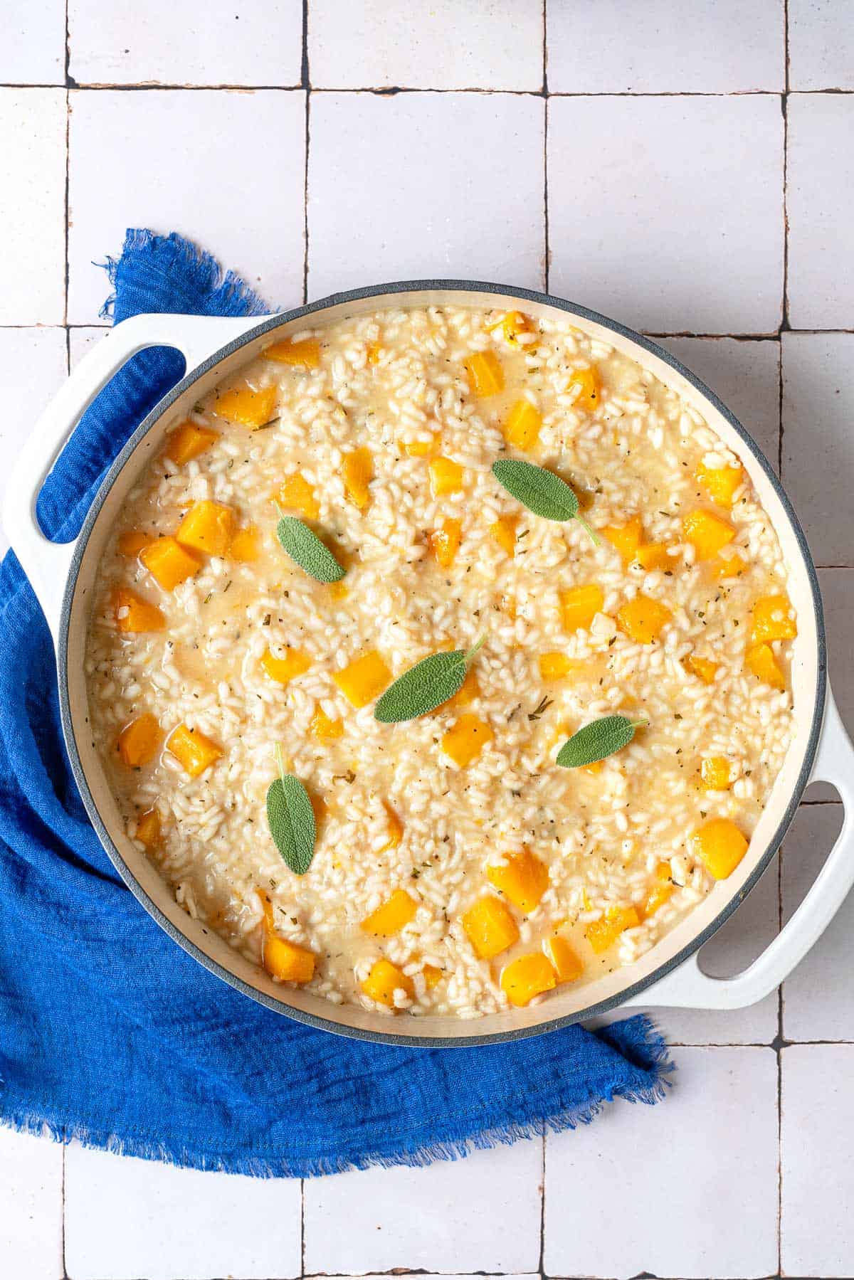 overhead photo of butternut squash risotto topped with sage leaves in a pot next to a blue linen napkin.