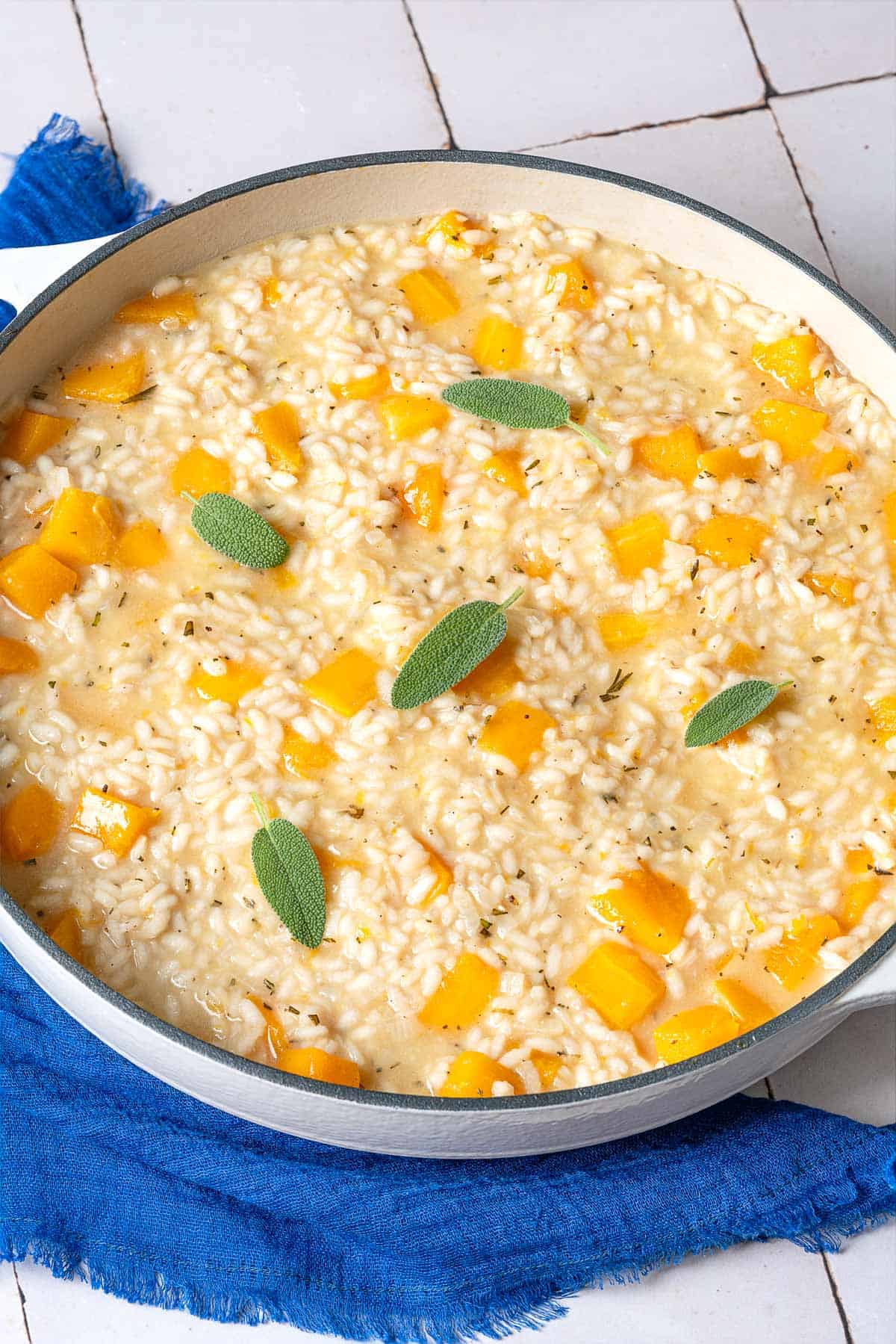 butternut squash risotto topped with sage leaves in a pot next to a blue linen napkin.