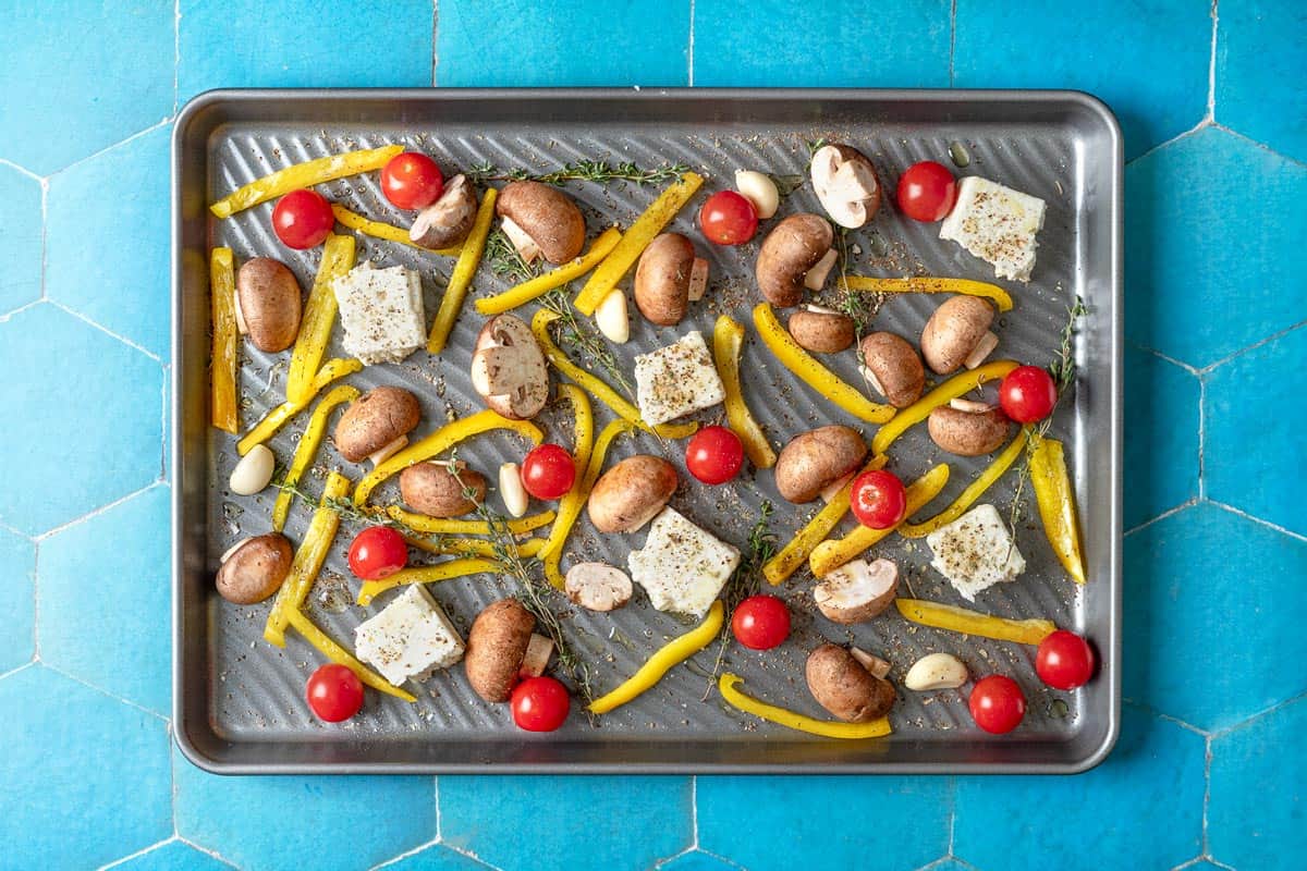 uncooked vegetables, feta and spices on a sheet pan.
