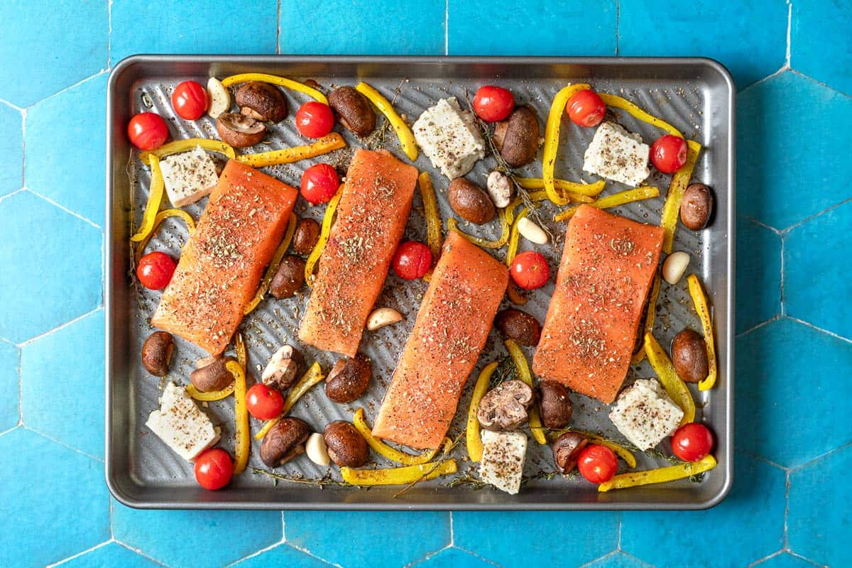 uncooked salmon fillets with vegetables and feta on a sheet pan.