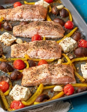 cooke baked salmon fillets with vegetables and feta on a sheet pan sitting on a white linen napkin.