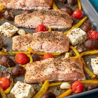 cooke baked salmon fillets with vegetables and feta on a sheet pan sitting on a white linen napkin.