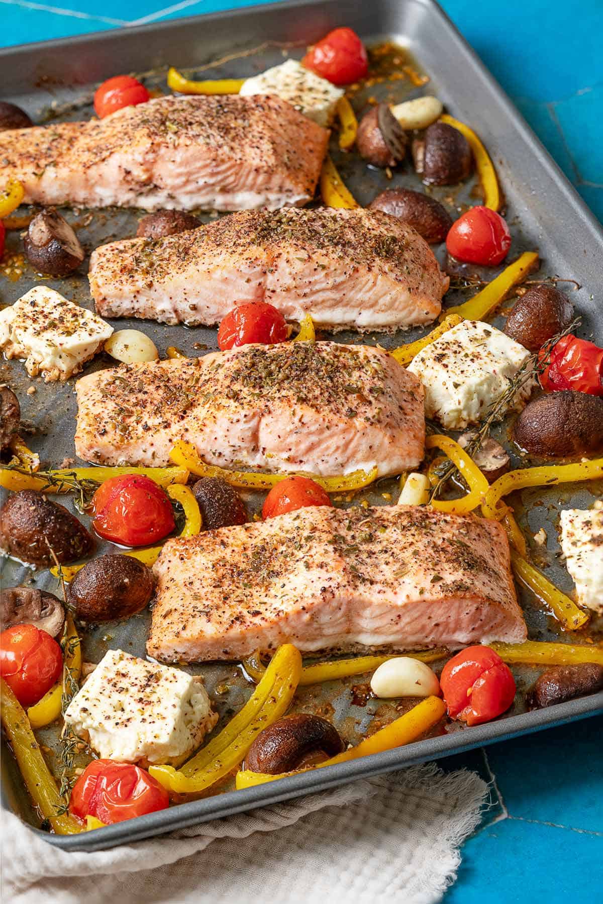 cooke baked salmon fillets with vegetables and feta on a sheet pan sitting on a white linen napkin.