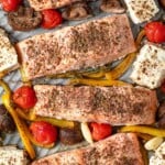 a close up of cooked baked salmon fillets with vegetables and feta on a sheet pan.