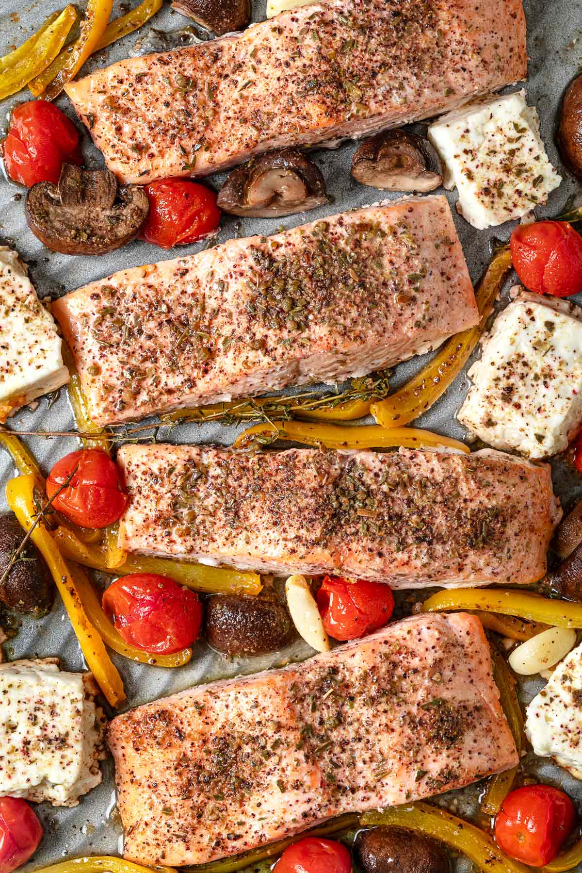 a close up of cooked baked salmon fillets with vegetables and feta on a sheet pan.