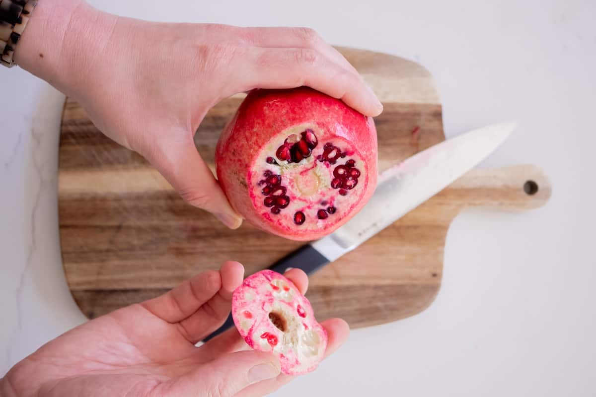 a close up of the top being removed from a pomegranate with a hand after cutting.