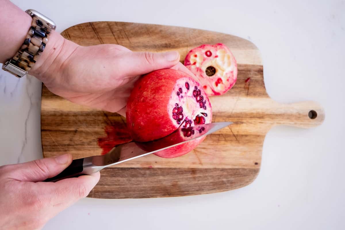 a close up of a knife being used to cut a pomegranate into sections.