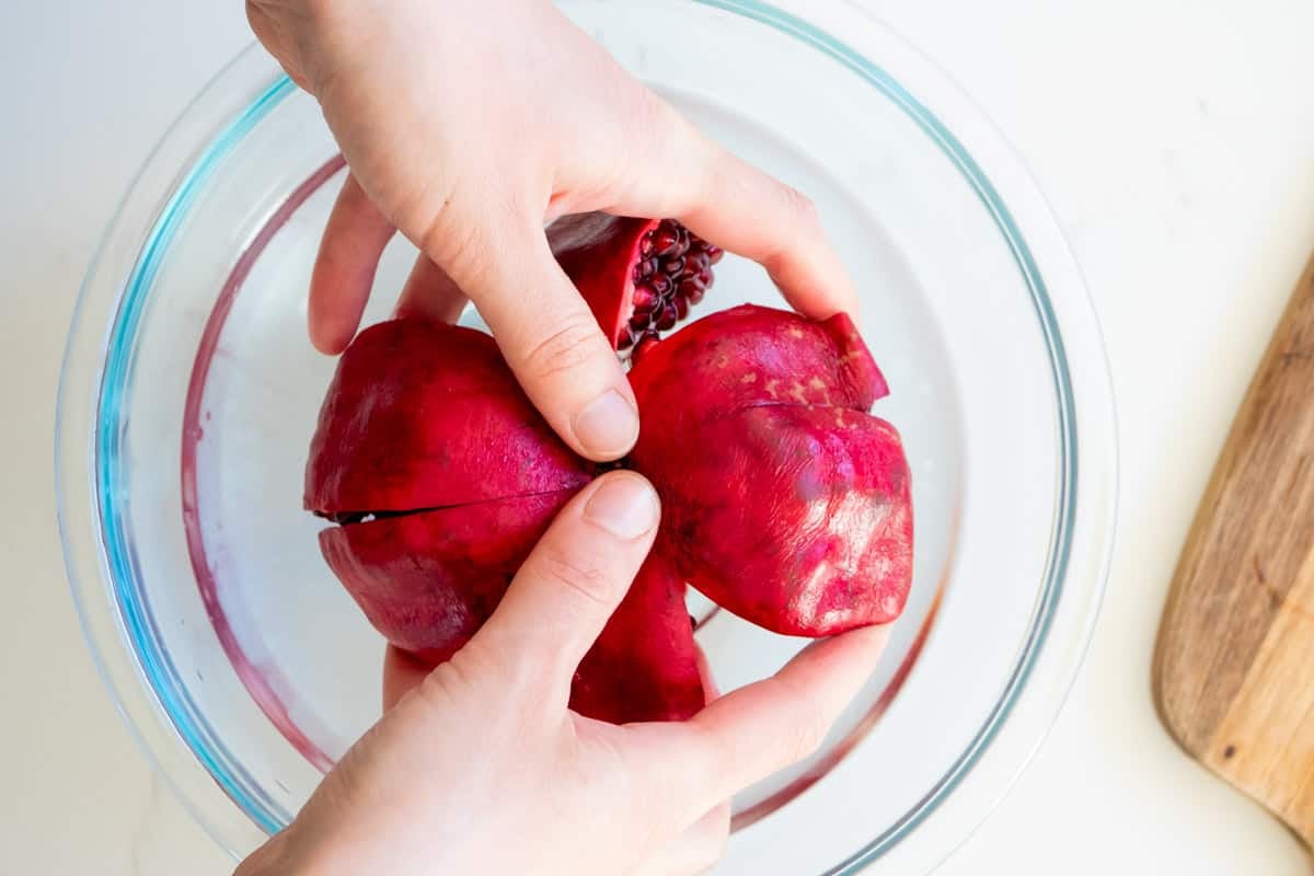 pomegranate sections being pulled apart over a bowl of cold water.