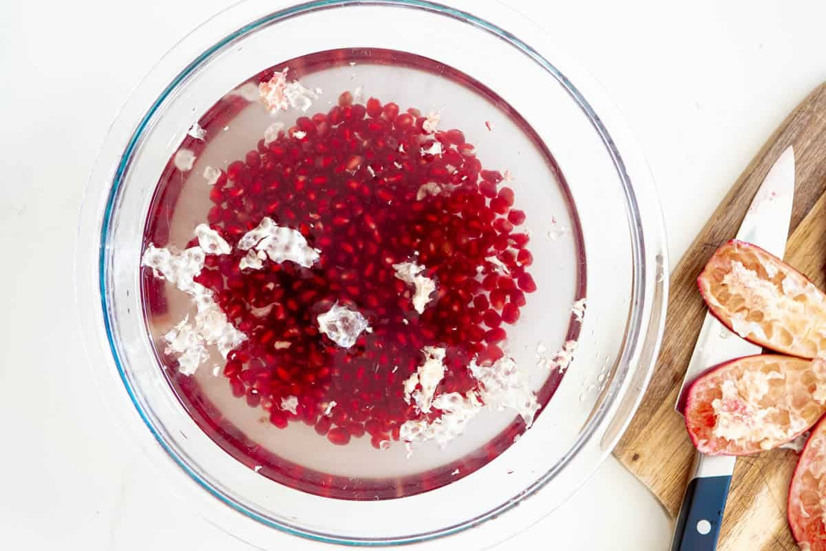 pomegranate seeds in a bowl of cold water with a bit of the pith floating on top.