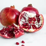 a close up of 3 pomegranates, two whole and one sectioned exposing the inside.