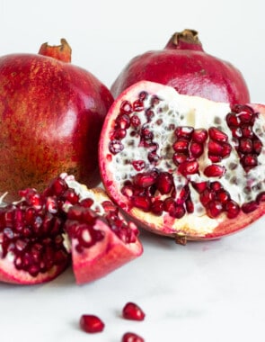 a close up of 3 pomegranates, two whole and one sectioned exposing the inside.