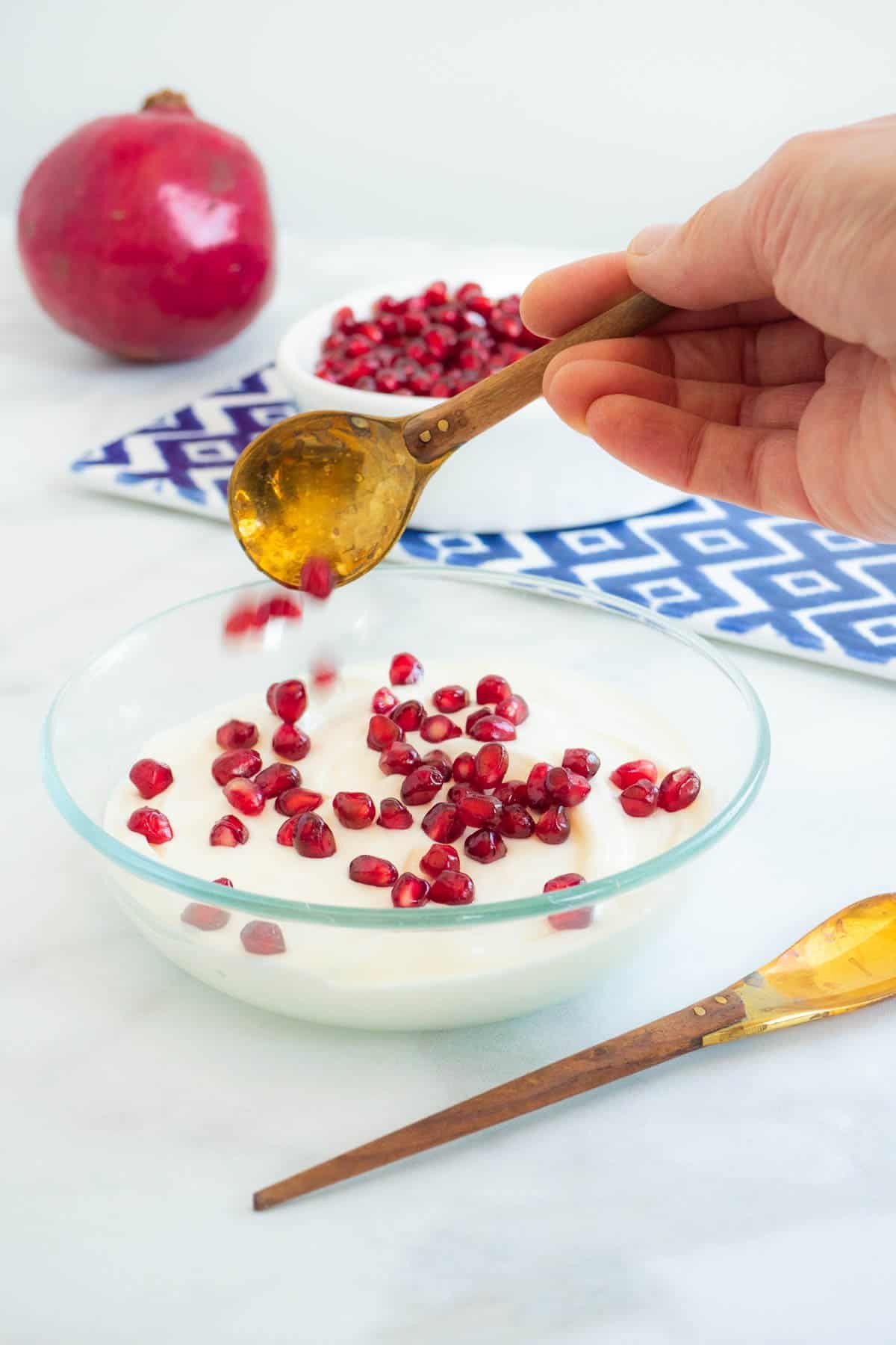 pomegranate seeds being sprinkled on some Greek yogurt in a bowl with a spoon.