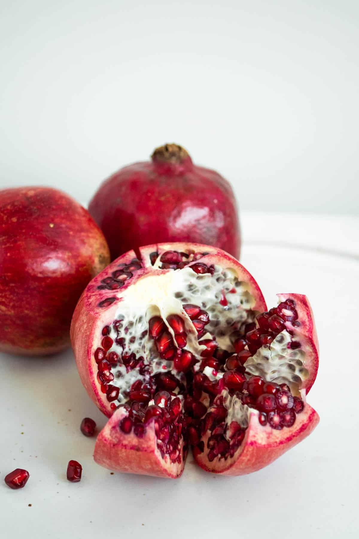 a close up of 3 pomegranates, two whole and one sectioned exposing the inside.