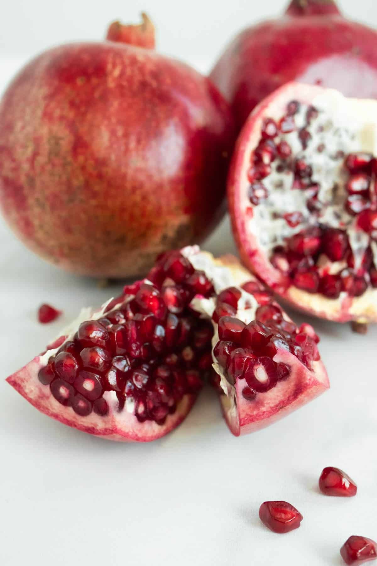 a close up of 3 pomegranates, two whole and one sectioned exposing the inside.