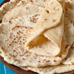 A stack of lavash bread in a wooden bowl. The top lavash is folded in a wrap shape, showing its flexibility.