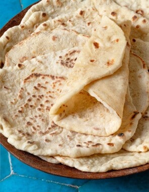 A stack of lavash bread in a wooden bowl. The top lavash is folded in a wrap shape, showing its flexibility.