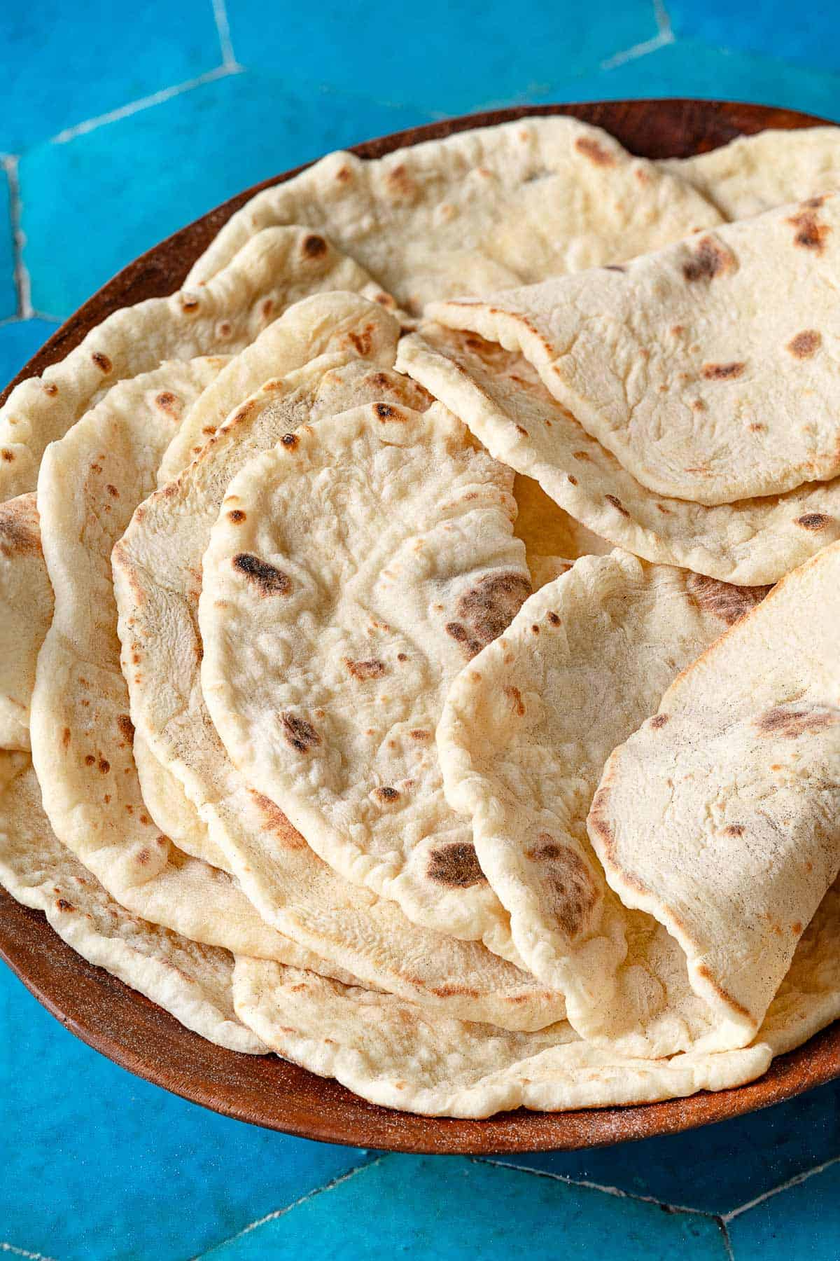 A stack of lavash bread in a wooden bowl. Each one is folded in half, showing their flexibility.