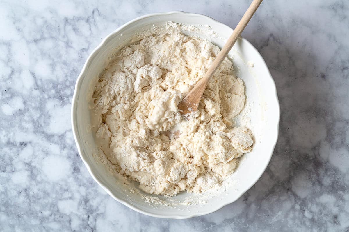 Milk and water being incorporated into the lavash dough in a white bowl with a wooden spoon.