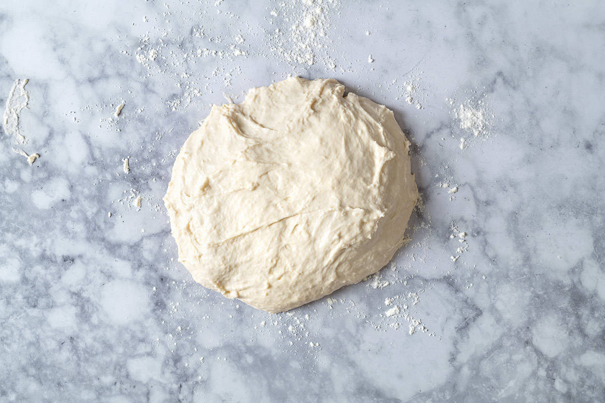 Lavash dough that has been kneaded on a flour-dusted marble slab, showing how sticky it is.