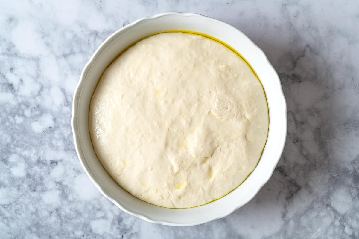 Lavash bread dough that has risen in a bowl, showing the growth and the coating of olive oil on top.